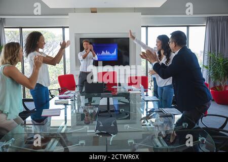 Multi-ethnic group of male and female business colleagues standing and clapping at the end of a meeting, celebrating success together. Creative busine Stock Photo
