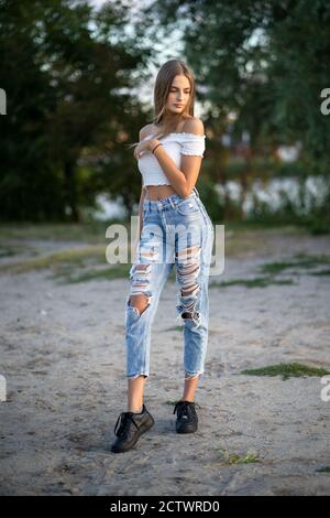 Young fashion model posing in nature on blurred background. Pretty girl in ripped blue jeans and white top. High quality photo Stock Photo