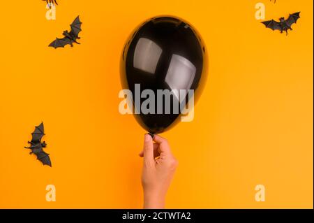 Bats and a black balloon in hand on an orange background. Halloween decor. Copy space. High quality photo Stock Photo