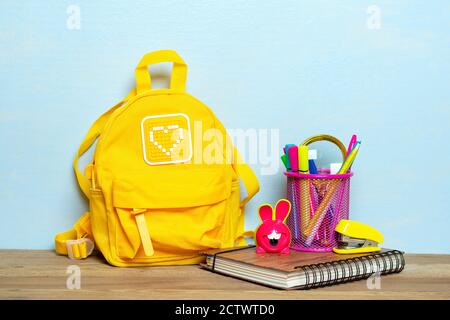 Back to school composition, education concept. Yellow backpack with school supplies - notebook, pens, stapler, pencil, sharpener isolated on blue Stock Photo
