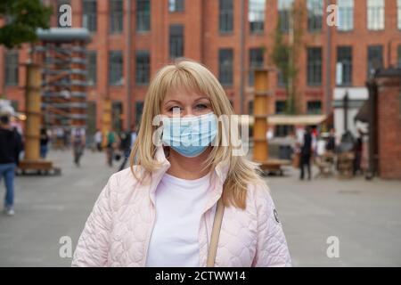 Woman in protective medical face mask standing outside in public place Stock Photo