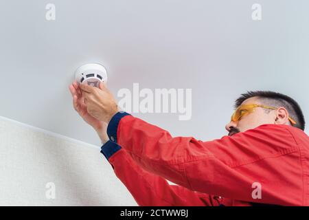 Worker installing smoke detector on the ceiling Stock Photo