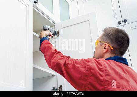 Worker using cordless screwdriver while installing new furniture in kitchen Stock Photo