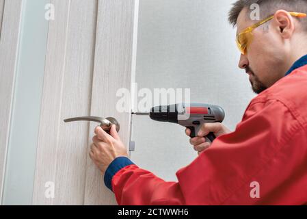 Worker installing or repairing the doorknob with screwdriver Stock Photo