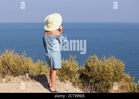 Woman in sun hat standing on mountain top on a blue sea background. Beach vacation, relax and dreaming concept Stock Photo