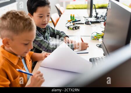 Selective focus of multiethnic schoolboys with notebooks sitting near computers in stem school Stock Photo