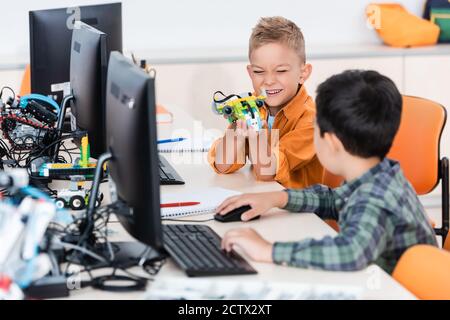 Selective focus of multiethnic schoolings playing with robot near computers in stem school Stock Photo