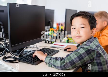 Selective focus of asian schoolboy looking at camera while using computer in classroom Stock Photo