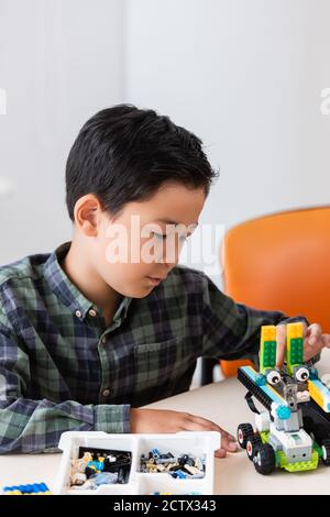 Selective focus of asian schoolboy looking at robot near building blocks on table in stem school Stock Photo