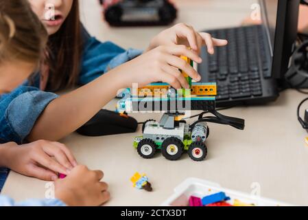 Selective focus of schoolgirls modeling robot from building blocks near computer in classroom Stock Photo