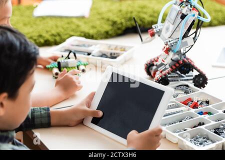 Selective focus of multiethnic pupils using digital tablet while constructing robot in classroom Stock Photo