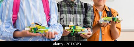 Panoramic crop of multiethnic schoolkids holding robots in classroom Stock Photo