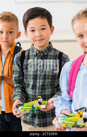 Selective focus of asian schoolboy holding robot near friends in school Stock Photo