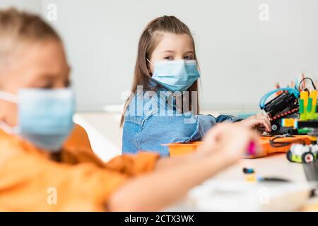 Selective focus of schoolkids in medical masks constructing robots in stem school Stock Photo
