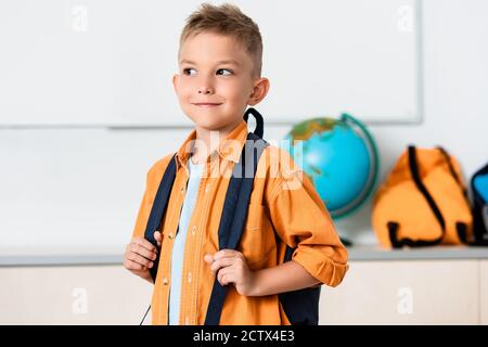 Schoolboy holding backpack while looking away in classroom Stock Photo