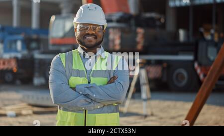 Portrait of Successful Contractor Investor Architectural Engineer Wearing Hard Hat and Safety Vest Standing on a Commercial Building Construction Site Stock Photo