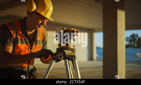 Inside of the Commercial Industrial Building Construction Site: Professional Engineer Surveyor Takes Measures with Theodolite, Using Digital Tablet Stock Photo