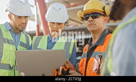 Diverse Team of Specialists Use Laptop Computer on Construction Site. Real Estate Building Project with Machinery: Civil Engineer, Investor Stock Photo