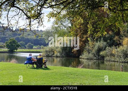 An elderly couple sitting by the River Thames at Runnymede on a late summers day, Egham Surrey England UK Stock Photo