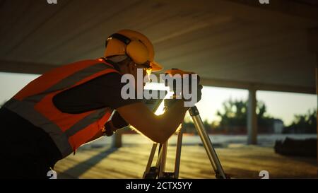 Inside of the Commercial Industrial Building Construction Site: Professional Engineer Surveyor Takes Measures with Theodolite, Using Digital Tablet Stock Photo