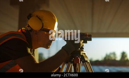 Inside of the Commercial Industrial Building Construction Site: Professional Engineer Surveyor Takes Measures with Theodolite, Using Digital Tablet Stock Photo