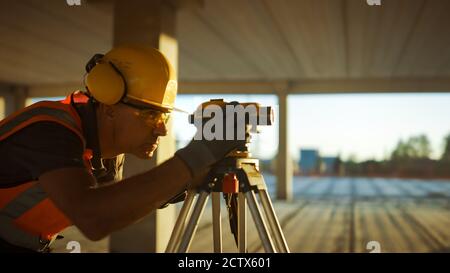 Inside of the Commercial Industrial Building Construction Site: Professional Engineer Surveyor Takes Measures with Theodolite, Using Digital Tablet Stock Photo