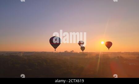 Aerial drone view of colorful hot air balloons flying over green park and river in small european city at summer sunrise, Kiev region, Ukraine Stock Photo
