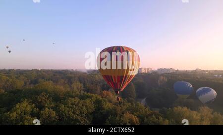 Aerial drone view of colorful hot air balloon flying over green park in small european city at summer sunrise, Kiev region, Ukraine Stock Photo