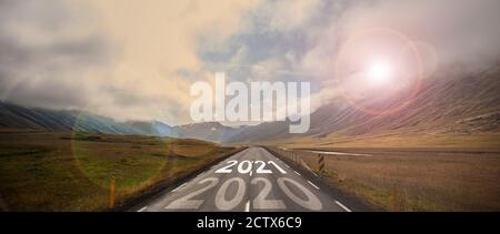 The word 2021 written on highway road in the middle of empty asphalt road at golden sunset and beautiful blue sky. Stock Photo