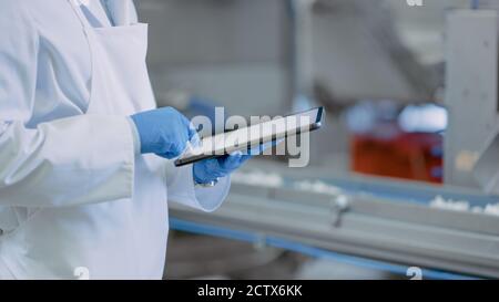 Quality Supervisor or Food Technician is Inspecting the Automated Production at a Food Factory. Close Up Shot of Employee Using Tablet Computer for Stock Photo