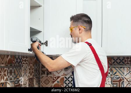 Maintenance worker using electric screwdriver while installing new furniture in kitchen. Contractor repairman assembling furniture Stock Photo