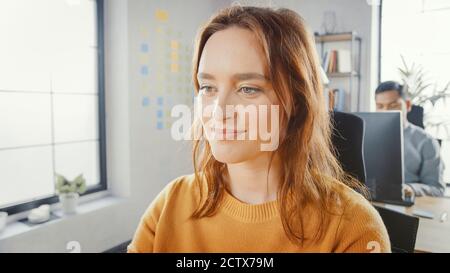 Portrait Shot of Beautiful Young Female Specialist Sitting at Her Desk Working on Desktop Computer. Diverse and Modern Office with Professionals Doing Stock Photo