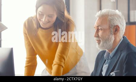 Handsome Senior Creative Engineer Sitting at the Desk working on Desktop Computer Has Discussion with Beautiful Female Project Manager. Office with Stock Photo