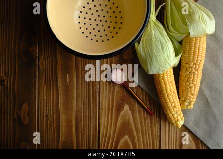 Closeup shot of fresh corns with husk tied up and a spoon full of white sugar on a wooden surface Stock Photo