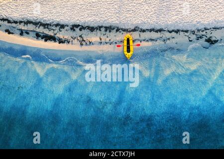 Yellow packraft rubber boat with red padle and turquoise water waves from top view. Beach with yellow sand glowing by sunlight. Travel summer vacations seascape background from drone Stock Photo