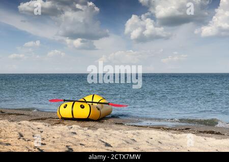 Yellow packraft rubber boat with red padle on a sea coast. Packrafting. Active lifestile concept Stock Photo