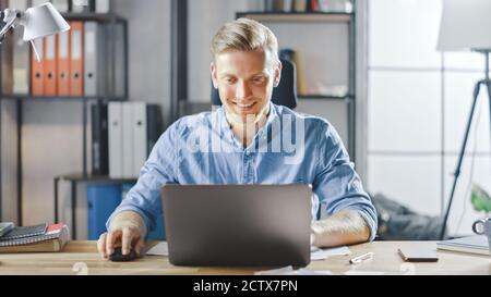 Handsome Blonde Businessman Sitting at His Desk in the Office Works on a Laptop. Creative Entrepreneur Using Computer Working on Software Unicorn Stock Photo