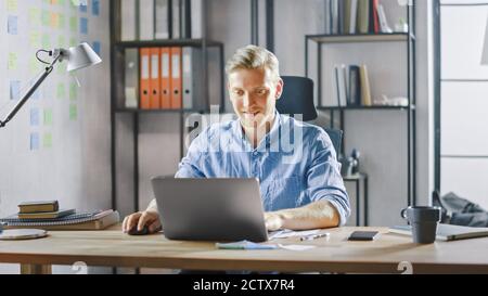 Handsome Blonde Businessman Sitting at His Desk in the Office Works on a Laptop. Creative Entrepreneur Using Computer Working on Software Unicorn Stock Photo