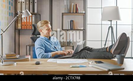 Handsome Young Entrepreneur Works on a Laptop with His Legs Up on the Desk. Designer Uses Notebook to Create Software Unicorn Startup. Chill Student Stock Photo