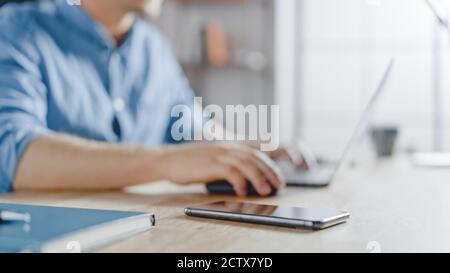 Close-up Shot of a Businessman Sitting at His Desk Works on Desktop Computer in the Stylish Office. His Smartphone Lies Near Him. Stock Photo