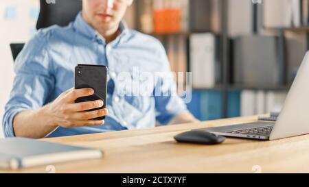 Businessman Sitting at His Desk Works on Desktop Computer in the Stylish Office and Using Smartphone, Uses Social Media App, Emailing Business Stock Photo