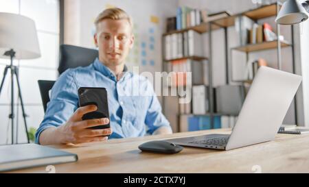 Businessman Sitting at His Desk Works on Desktop Computer in the Stylish Office, Picks up and Starts Using Smartphone, Uses Social Media App, Emailing Stock Photo