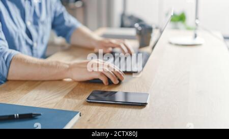 Close-up Shot of a Businessman Sitting at His Desk Works on Desktop Computer in the Stylish Office. His Smartphone Lies Near Him. Stock Photo