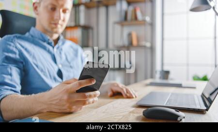Businessman Sitting at His Desk Works on Desktop Computer in the Stylish Office, Picks up and Starts Using Smartphone, Uses Social Media App, Emailing Stock Photo