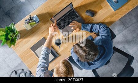 Top View Shot of a Young Businessman Working at His Desk on a Laptop, Talks with His Manager and Listens to a Advice on the Project Concept. Two Men Stock Photo