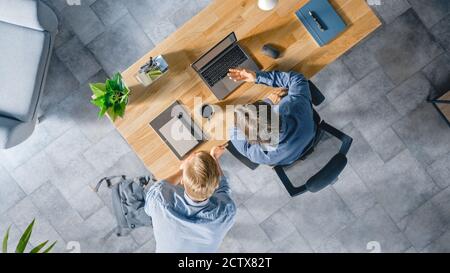 Top View Shot of a Young Businessman Working at His Desk on a Laptop, Talks with His Manager and Listens to a Advice on the Project Concept. Two Men Stock Photo