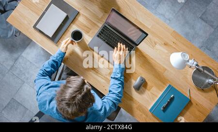 In the Office Businessman Sitting at the Wooden Desk Works on a Laptop in his Home Office. He Drinks Coffee, Types, Writes Emails, Surfs the Internet Stock Photo
