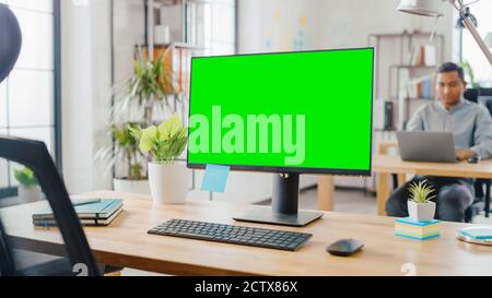 Mock-up Screen Desktop Computer Standing on the Desk in the Modern Creative Office. In the Background Bright Studio Apartment where Diverse Team of Stock Photo