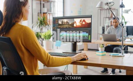 Over the Shoulder: Creative Young Woman Works with Footage on Her Personal Computer with Big Display. In the Background Bright Office where Diverse Stock Photo