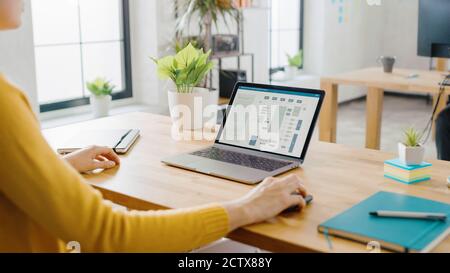 Over the Shoulder: Female Engineer Developer Sitting at Her Desk Using Laptop with Hardware Microchip Design. Office where Diverse Team of Young Stock Photo